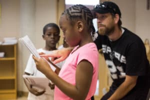 Trinity Gilchrist, 8, center, reads a story she wrote while her teacher, Jason Harrison, right, helps her during The Serna Summer Enrichment Program. WENDI POOLE / SPECIAL TO FOLO MEDIA